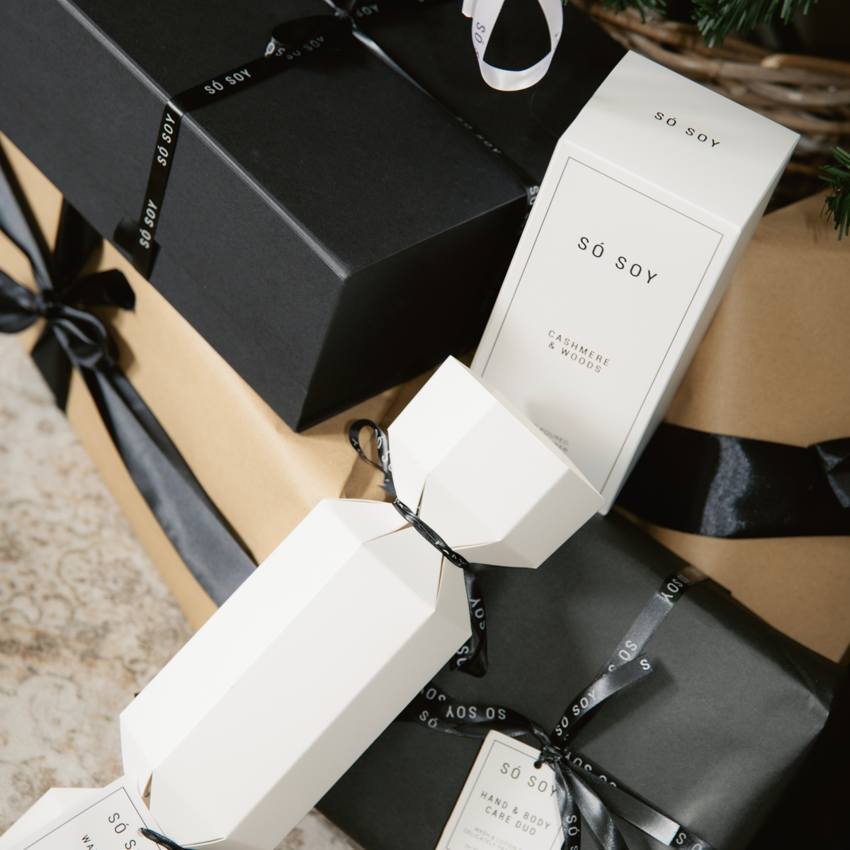 White and black SÓ Soy gift packaging arranged on wrapped presents with black ribbon bows.