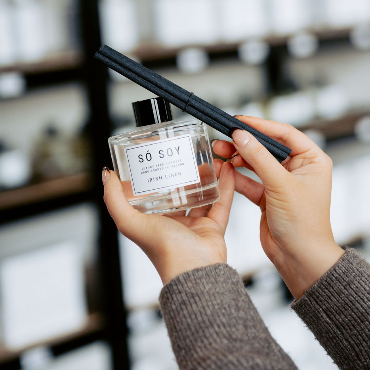 Person holding a diffuser bottle labeled 'Soy' in a store setting.